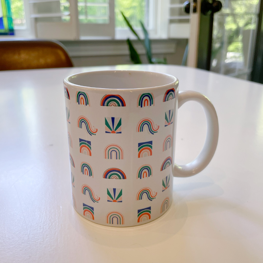 White coffee mug with with cute rainbow illustrations sitting on a table