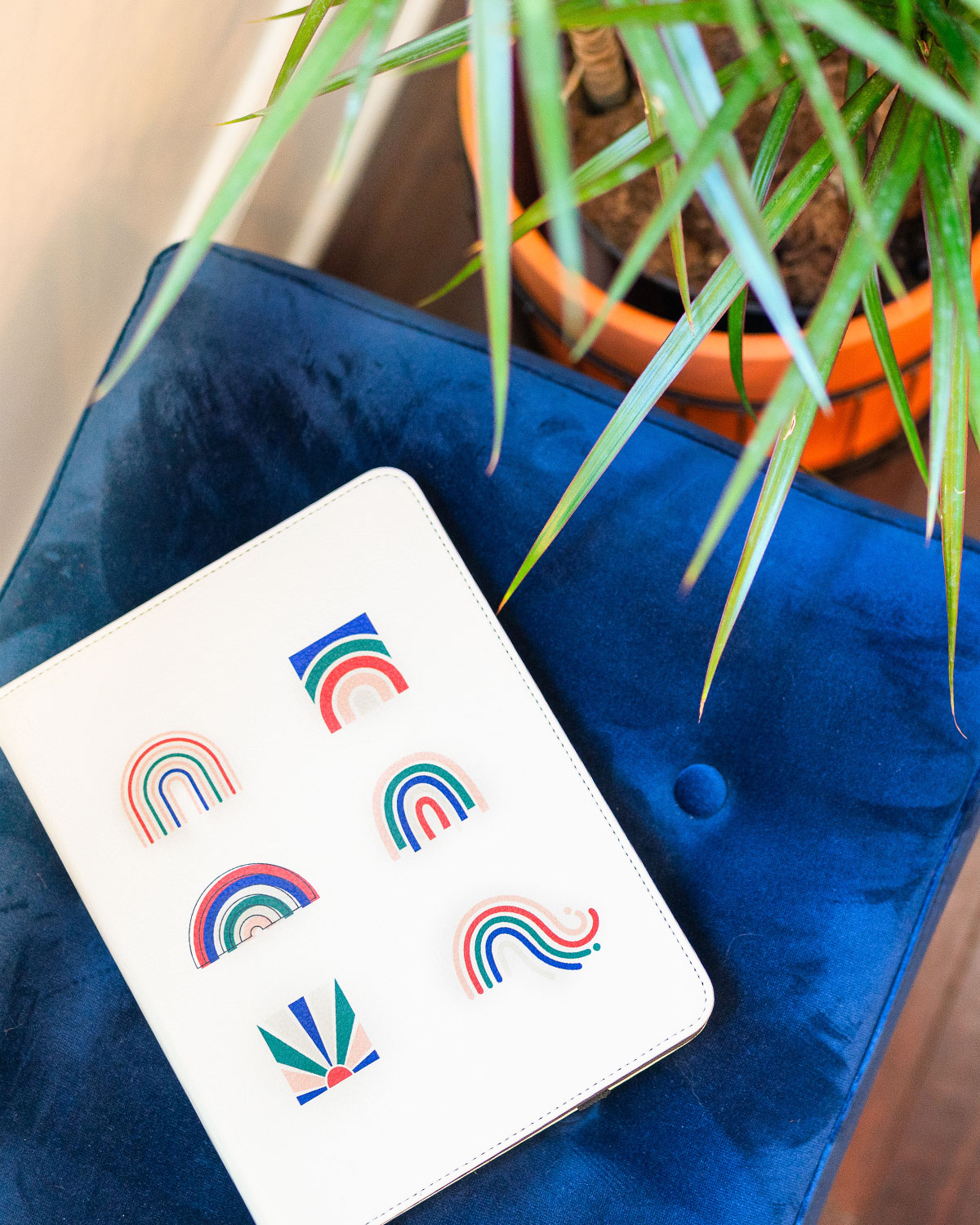 iPad cover with cute rainbow designs on a blue chair with a plant in the background